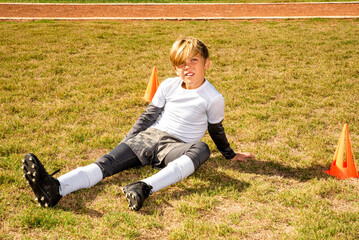Young boy soccer player sitting in the grass after falling down on the field