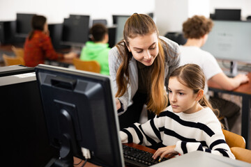 Female teacher and her student, young girl, looking at monitor of PC during computer science lesson.