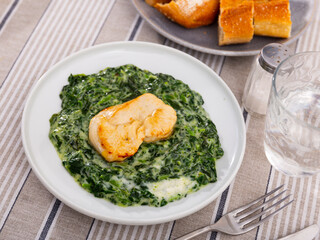 Delicious golden roasted chicken breast with side dish of spinach in creamy white sauce bechamel