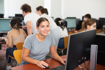 Smiling female student using PC and studying computer science in the classroom