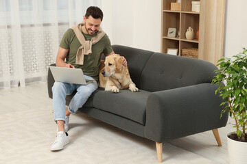 Man using laptop on sofa near his cute Labrador Retriever at home. Space for text