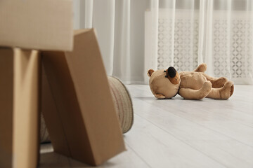 Cute lonely teddy bear on floor near boxes indoors