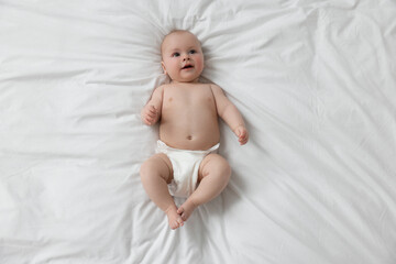 Cute little baby in diaper lying on white bed, top view