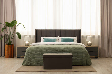 Comfortable bed, bedside tables and ottoman in bedroom