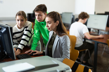Fototapeta na wymiar Modern interested teen schoolchildren learning basics of programming with friendly female teacher in computer college..
