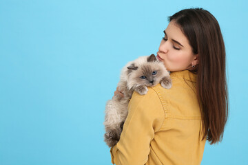 Woman kissing her cute cat on light blue background, space for text