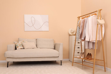Fototapeta na wymiar Stylish living room interior with comfortable sofa and clothing rack