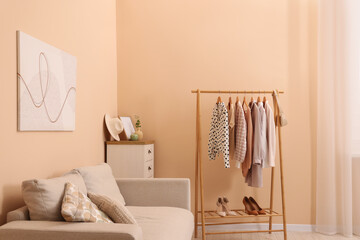 Stylish living room interior with comfortable sofa and clothing rack
