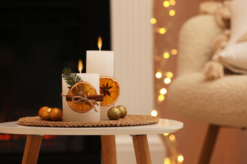 Beautiful burning candles decorated with dry orange slices and cinnamon sticks on white table indoors. Christmas atmosphere