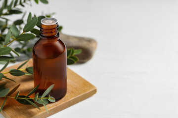 Bottle of eucalyptus essential oil and plant branches on white table, space for text