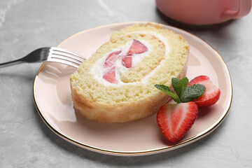Slice of delicious sponge cake roll with strawberries and cream served on light grey table, closeup
