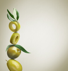 Cut and whole green olives with leaves on dusty beige background, space for text