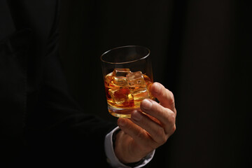 Man holding glass of whiskey with ice cubes on dark background, closeup