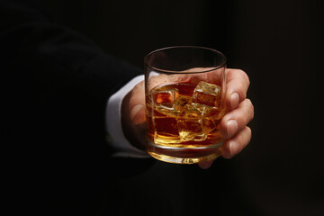 Man holding glass of whiskey with ice cubes on dark background, closeup