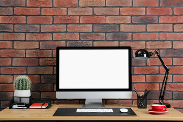 Fototapeta premium Stylish workplace with computer, lamp and stationery on wooden table near brick wall