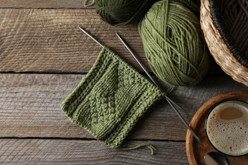 Soft green woolen yarn, knitting, needles and glass of drink on wooden table, flat lay. Space for...