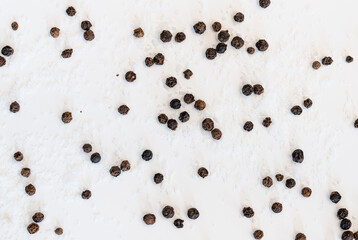 Table salt and black peppercorns scattered on a white background