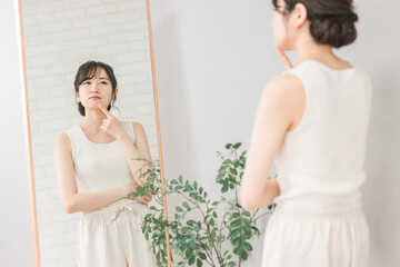 ニキビ・肌荒れ・吹き出物に悩む鏡を見るアジア人女性
