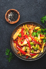 Asian cuisine, stir fry chicken, red paprika and zucchini with sesame and soy sauce in bowl. Black table background, top view, copy space