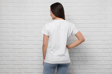 Woman wearing stylish T-shirt near white brick wall, back view