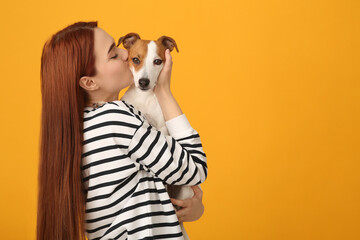 Woman kissing cute Jack Russell Terrier dog on orange background. Space for text