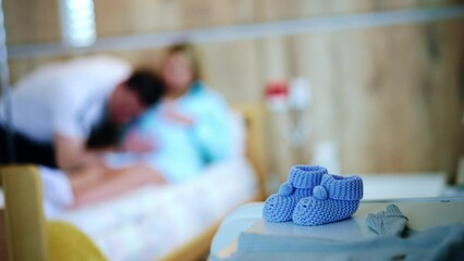 Little blue knitted socks prepared for newborn. Couple expecting child at backdrop in blur. - Powered by Adobe