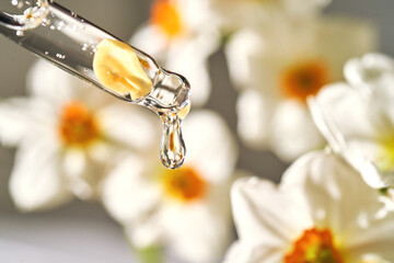 An eyedropper with a cosmetic product on the flower background.