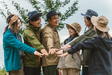 秋冬のキャンプ場で仲間と一致団結して円陣を組む男女（友情・友達・チームワーク・アウトドア）
