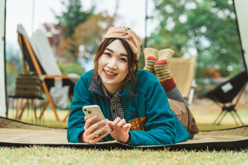秋冬のキャンプ・アウトドアでスマホを使う若いアジア人女性キャンパー
