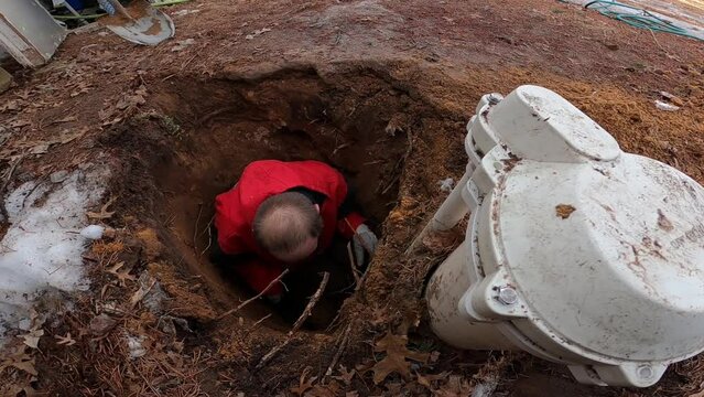 Man in hole next to water well trying to reach some parts to fix water pressure issue or other pump problems.