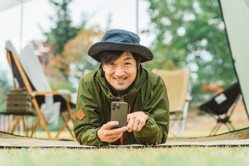 秋冬のキャンプ・アウトドアでスマホを使う若いアジア人男性キャンパー
