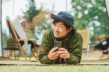 秋冬のキャンプ・アウトドアでスマホを使う若いアジア人男性キャンパー
