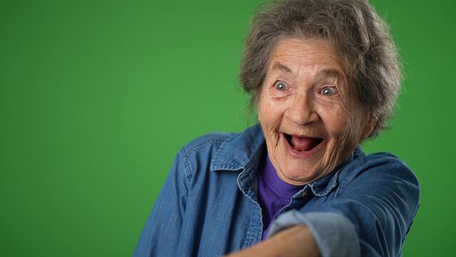Closeup funny crazy portrait of happy elderly senior old woman with wrinkled skin and grey hair smiling and look around for friend find meet greet someone posing on green screen background. - Powered by Adobe