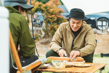 キャンプ飯を仲間と食べるアジア人男性キャンパー
