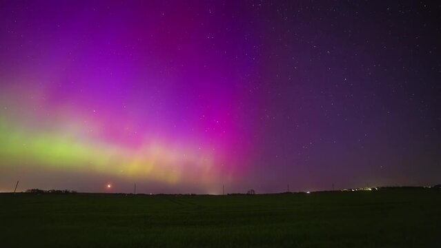 The green and yellow Northern Lights dance in a purple sky during a rising moon. Time lapse
