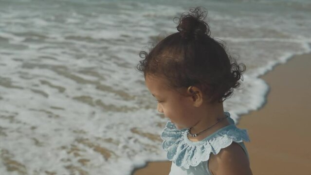 Semi-close up shot of Indian child in light blue dress watching calm waves at Benaulim Beach, Goa