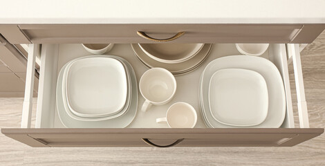 Open drawer with clean dishes and cups in kitchen, top view