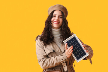 Teenage girl in beret with portable solar panel on yellow background