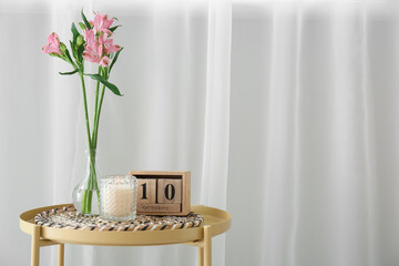 Vase with beautiful alstroemeria flowers, burning candle in holder and cube calendar with date 10th OCTOBER near white curtain