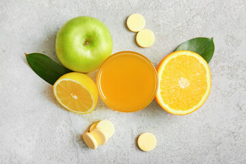 Glass of vitamin C effervescent tablet dissolved in water and fruits on grey grunge table