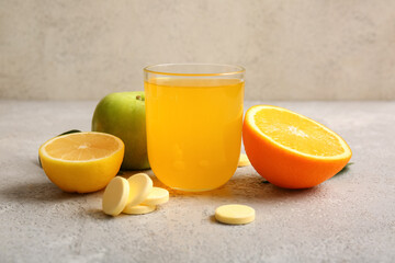 Glass of vitamin C effervescent tablet dissolved in water and fruits on grey grunge table