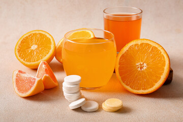 Glasses of vitamin C effervescent tablet dissolved in water and fruits on grey grunge table