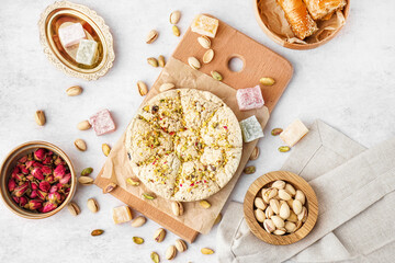 Wooden board of tasty Tahini halva with pistachios on light background