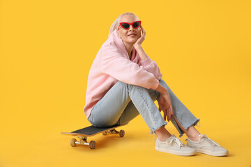 Mature woman with skateboard sitting on yellow background © Pixel-Shot
