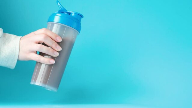 Female hand shakes shaker with chocolate protein cocktail on blue background.