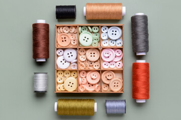 Fototapeta na wymiar Composition with box of different buttons and thread spools on grey background