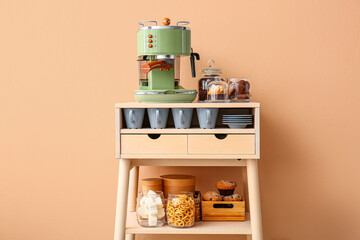 Table with coffee machine, snacks and cups near beige wall