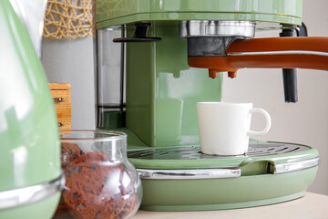 Modern coffee machine, cups and jar with cookies on table near white wall, closeup