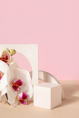 Decorative plaster podiums and beautiful orchid flowers on beige table against pink background