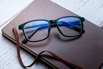 black frame blue light blocking technology anti glare spectacles glasses on brown textured book...